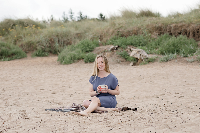 Dr Kate Ella sitting on the beach with a cup of tea